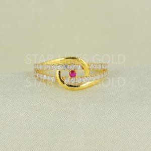Pode incluir: Um anel de ouro com uma pedra vermelha no centro e uma fileira de pedras transparentes ao redor da banda.