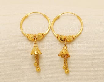 May include: A pair of gold-colored hoop earrings. Each earring features a circular hoop with decorative elements and a dangling bell-shaped charm with three small, round accents. The earrings are displayed on a white surface.