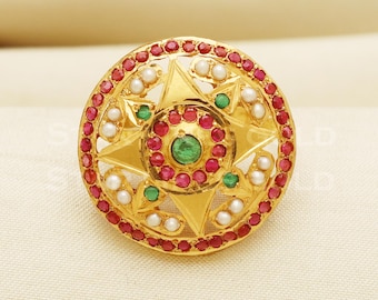 May include: A gold ring with a circular design featuring a star shape with red and green gemstones and white pearls around the edge.