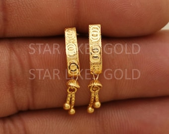 May include: A pair of gold-colored hoop earrings. The earrings have a detailed pattern and small dangling accents with tiny gold spheres. The text "STAR GOLD" is visible on the earrings.