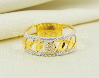 May include: A gold ring with a leaf design and a band of small, clear stones. The ring has a floral design in the center and is set against a cream-colored background. The ring is a piece of jewelry.