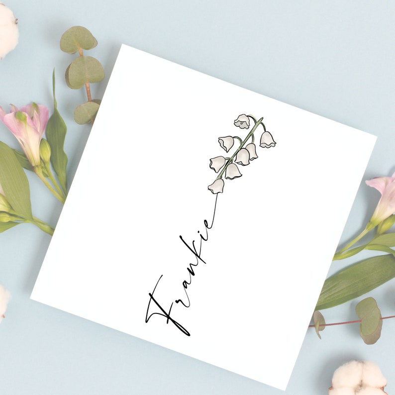 May include: A white card with a black cursive name "Frankie" and a drawing of a white lily of the valley flower with green stems.
