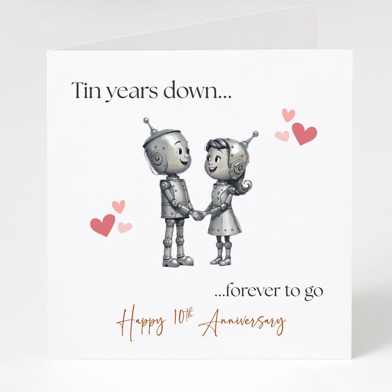 May include: A white greeting card with the text "Tin years down... ...forever to go Happy 10th Anniversary." The card features two robot figures holding hands, with pink hearts scattered around them.