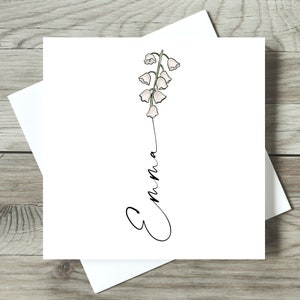 May include: A white card with a black and green illustration of a lily of the valley flower. The name "Emma" is written in cursive below the flower.