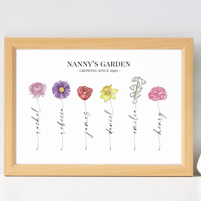 May include: A white framed print with the text "Nanny's Garden - Growing Since 1990 -" and a line of flowers with names written underneath each flower. The flowers are a purple chrysanthemum, a purple aster, a red rose, a yellow daffodil, a white lily of the valley, and a pink carnation. The names are Rachel, Rebecca, James, Daniel, Emilia, and Henry.