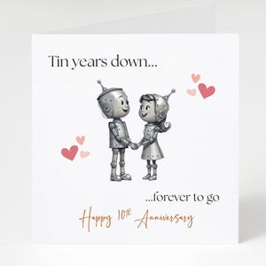 May include: A white greeting card with the text "Tin years down... ...forever to go Happy 10th Anniversary." The card features two robot figures holding hands, with pink hearts scattered around them.
