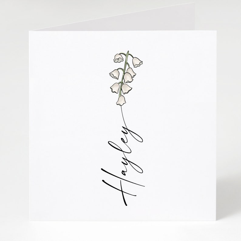 May include: A white card with a simple line drawing of a lily of the valley flower and the name "Hayley" written in cursive.