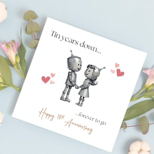 May include: A white anniversary card with the text "Tin years down..." and "...forever to go". The card features a cartoon illustration of two robots holding hands, with pink hearts. The text "Happy 10th Anniversary" is also on the card.