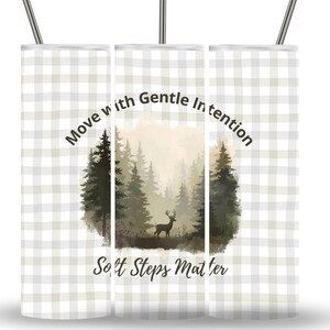 Könnte beinhalten: Ein Edelstahlbecher mit einem grau-weißen Karomuster. Der Becher zeigt eine Waldszene mit einem Hirsch und dem Text "Move with Gentle Intention" und "Soft Steps Matter".