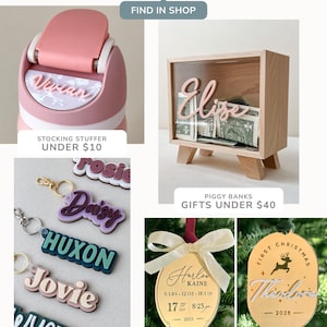 May include: A collection of personalized items including a pink water bottle with the name Vivian, a wooden shadow box piggy bank labeled Elise, layered acrylic keychains with names, and gold-toned oval ornaments featuring birth details and names.