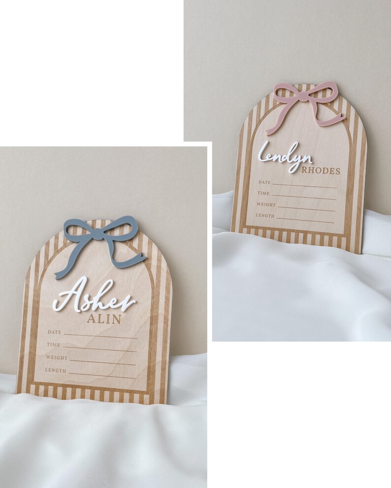 May include: Two arched wooden birth announcement signs with vertical stripes. One features a blue bow and the name Asher Alin, the other a pink bow and the name Lendyn Rhodes. Both include white 3D lettering and printed lines for date, time, weight, and length.