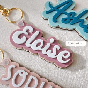 Puede incluir: Llaveros con nombres personalizados en varios colores. Los llaveros presentan nombres en letras blancas sobre un fondo de color, con un cierre dorado. El ancho de los llaveros es de 7,6-10,2 cm.