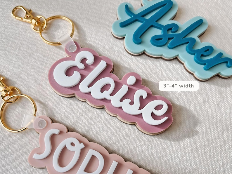 Puede incluir: Llaveros con nombres personalizados en varios colores. Los llaveros presentan nombres en letras blancas sobre un fondo de color, con un cierre dorado. El ancho de los llaveros es de 7,6-10,2 cm.