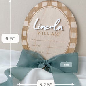 K&ouml;nnte beinhalten: Ein ovales Geburtsank&uuml;ndigungsschild aus Holz mit einer H&ouml;he von 16,51 cm und einer Breite von 13,34 cm. Es hat einen hellbraunen karierten Rand, den Namen Lincoln in erhabener wei&szlig;er Schreibschrift, WILLIAM in Braun sowie Leerzeilen f&uuml;r Datum, Uhrzeit, Gewicht und L&auml;nge. Ein blaugr&uuml;nes Band ist an der Basis gebunden.