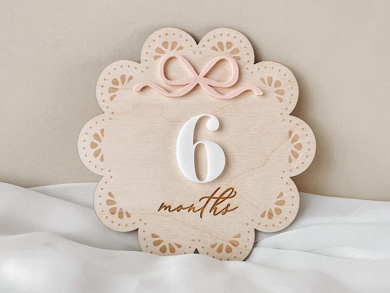 Crafted intricately from wood, the monthly milestone disc features a delicate bow and lace pattern, adding a charming touch to any baby girl's nursery.