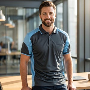 May include: A short-sleeved polo shirt featuring a dark gray center panel and light blue side panels, sleeves, and collar trim. The shirt includes a buttoned placket and a single chest pocket on the left side, constructed from a smooth fabric.
