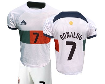 May include: White soccer jersey with green, red, and white stripes across the chest. The jersey has the number 7 on the front and the word "RONALDO" and the number 7 on the back. The jersey is paired with white shorts with the number 7 on the right leg.