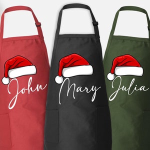 May include: Three red, black, and green aprons with a white Santa hat design and personalized names: John, Mary, and Julia.