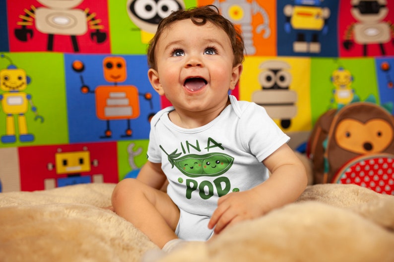 May include: A white baby onesie with a green pea pod design and the text "In a Pod."
