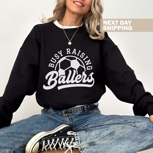 May include: Black sweatshirt with a white graphic that says "Busy Raising Ballers" with a soccer ball in the center.