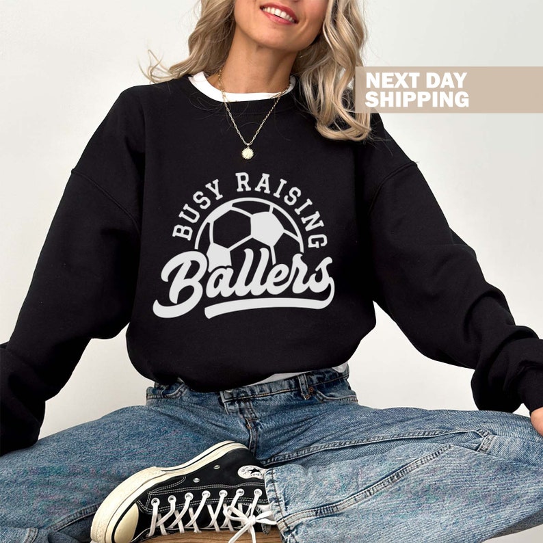 May include: Black sweatshirt with a white graphic that says "Busy Raising Ballers" with a soccer ball in the center.