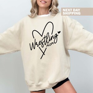 May include: A beige sweatshirt with a black heart design and the text "Wrestling Mom" inside the heart.