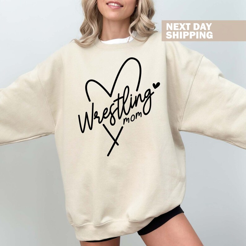 May include: A beige sweatshirt with a black heart design and the text "Wrestling Mom" inside the heart.