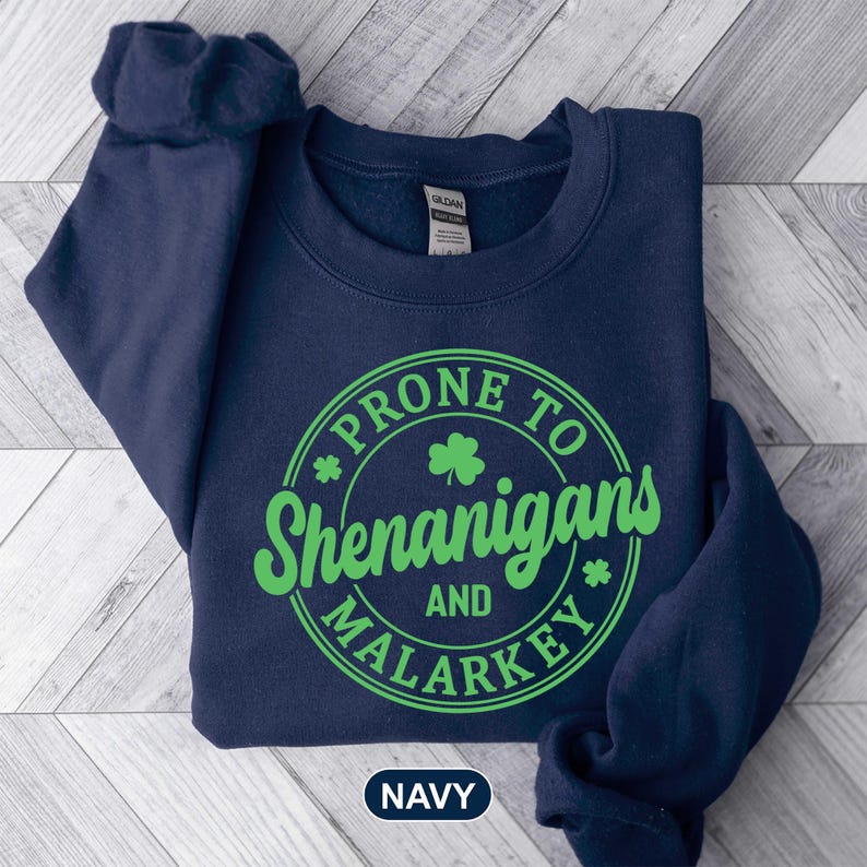 Puede incluir: Sudadera azul marino con un gr&aacute;fico circular verde que dice "Prone to Shenanigans and Malarkey".