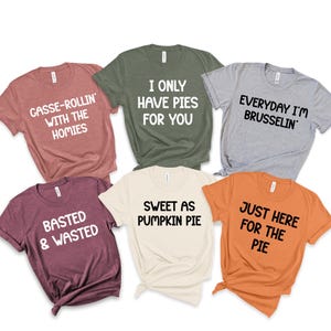 May include: A collection of six short-sleeved t-shirts in various colors, each with a unique text-based design. The shirts feature phrases like "CASSE-ROLLIN' WITH THE HOMIES" and "SWEET AS PUMPKIN PIE."