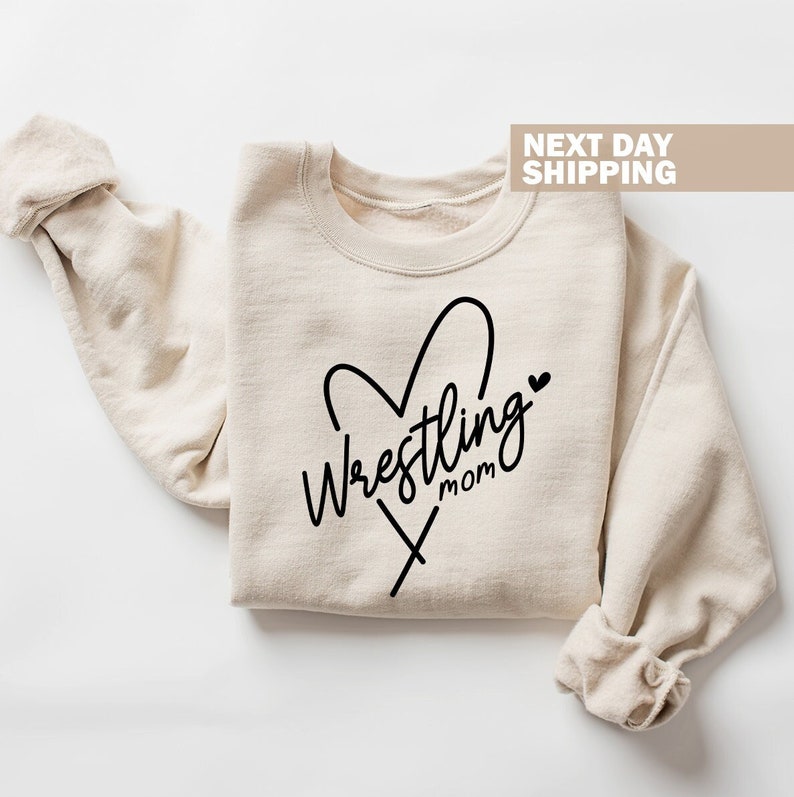 May include: A beige sweatshirt with a black heart and the text "Wrestling Mom" printed on the front.