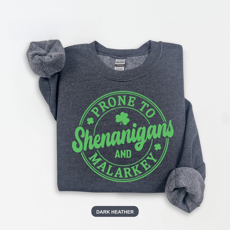 Puede incluir: Sudadera gris oscuro con un gr&aacute;fico circular verde que dice "Prone to Shenanigans and Malarkey" con un dise&ntilde;o de tr&eacute;bol.
