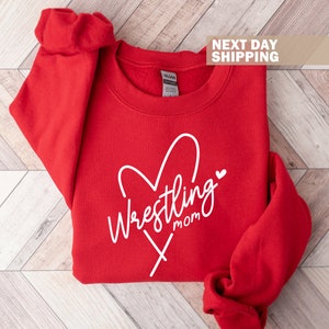May include: Red sweatshirt with a white heart and the text "Wrestling Mom" in a cursive font.