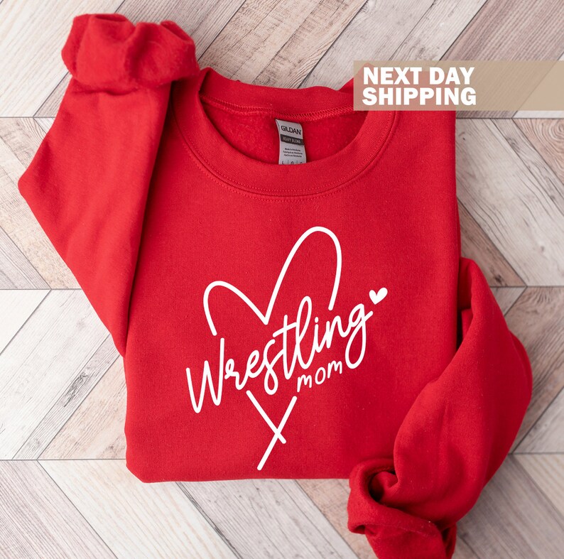 May include: Red sweatshirt with a white heart and the text "Wrestling Mom" in a cursive font.