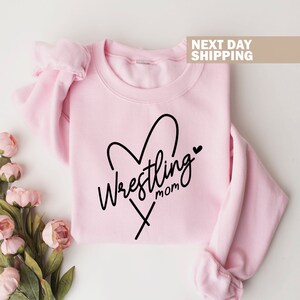 May include: Pink sweatshirt with a black heart design and the text "Wrestling Mom" inside the heart.