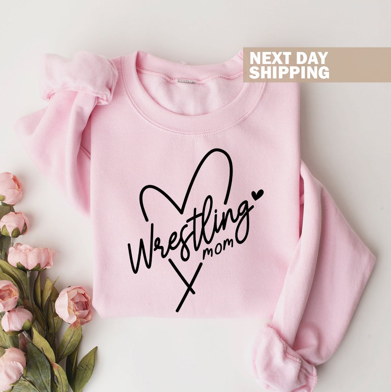 May include: Pink sweatshirt with a black heart design and the text "Wrestling Mom" inside the heart.