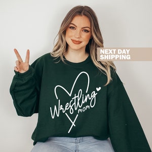 May include: A dark green sweatshirt with a white heart and the text "Wrestling Mom" inside the heart.