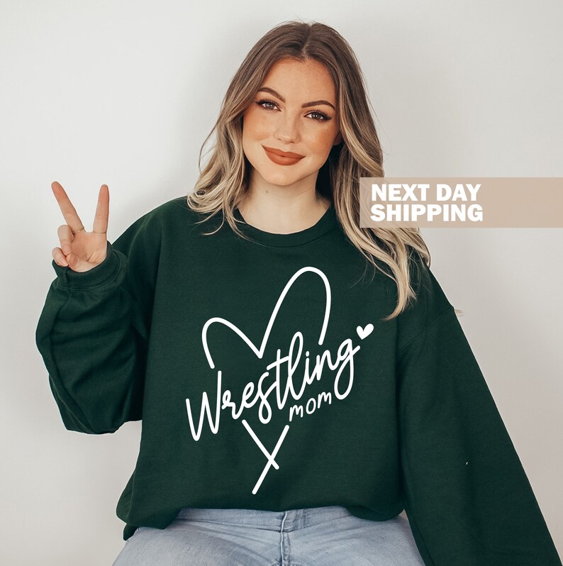 May include: A dark green sweatshirt with a white heart and the text "Wrestling Mom" inside the heart.