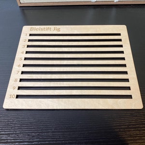 Puede incluir: Un jig de madera con el texto "Bleistift Jig" y líneas numeradas del 1 al 10.