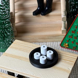 May include: Miniature scene with a black tray holding four white candles. Two black boots are on the wooden stairs in the background. A small Christmas tree and a green advent calendar are also visible.