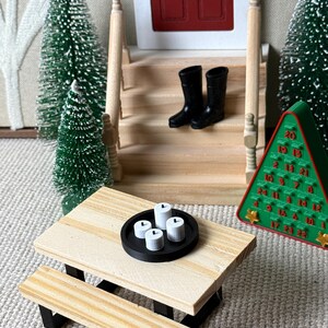 May include: Miniature Christmas scene with a wooden picnic table, black boots on steps, and a green advent calendar. The table holds a black tray with four white candles. Decorative miniature Christmas trees are also present.