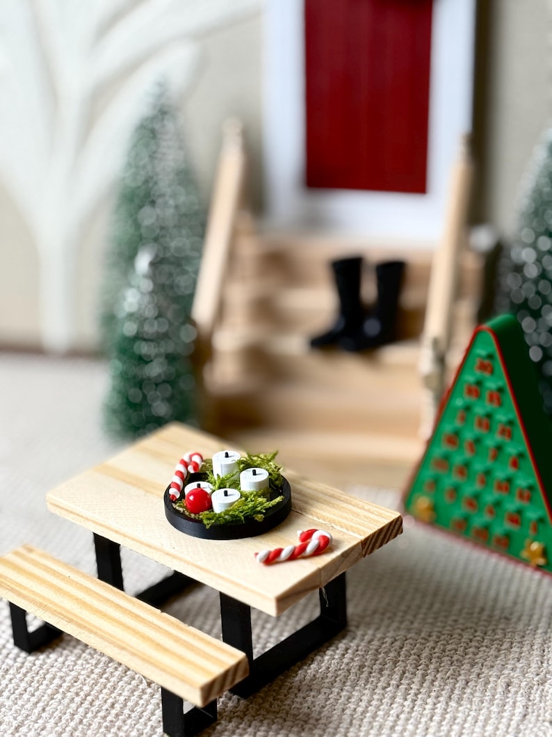 May include: Miniature Christmas scene featuring a wooden picnic table with a black base. A small black tray holds four white candles, red berries, and greenery. Two candy canes and a green Christmas tree are also visible.