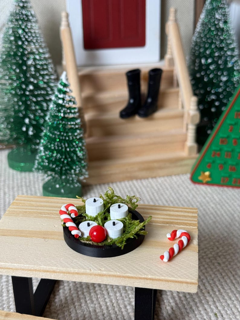 May include: Miniature Christmas scene with a small wooden table holding a black tray with white candles, a red ball, and green moss. Two candy canes and miniature black boots are also visible.