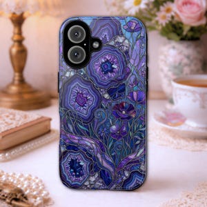 May include: A phone case featuring a stained-glass design with purple and blue floral and geode patterns. The case has a glossy finish and a camera cutout. The design includes intricate details and a variety of shades of purple and blue.