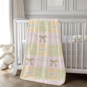 May include: A patchwork baby blanket with a mix of floral, plaid, and polka dot patterns in pastel pink, green, and beige. The blanket features the name "Olivia" and bow accents, draped over a white crib.