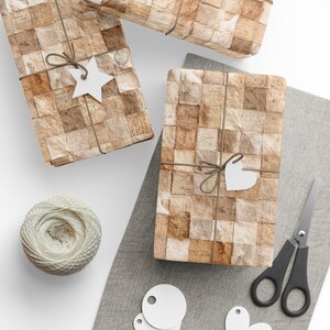 May include: Gift-wrapped presents with a vintage paper pattern, tied with twine and adorned with white star and heart-shaped tags. A ball of twine, scissors, and additional tags are arranged on a gray cloth, creating a scene of preparation.