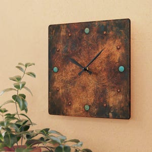 May include: A square wall clock with a dark, weathered copper-toned finish featuring an embossed floral pattern. The clock face is accented with small turquoise circular inlays and copper-colored studs, paired with simple black hour and minute hands.