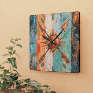 May include: A square wall clock featuring a distressed, multi-colored background of vertical stripes in shades of teal, orange, and white. The center displays a copper-toned sunburst design overlaid with two crossed arrows and black clock hands.
