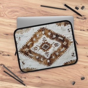 May include: A laptop sleeve with a white background and a brown geometric pattern. The pattern is a diamond shape with a smaller diamond in the center. The sleeve has a zipper on the side.