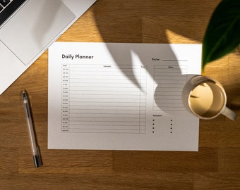 May include: A white daily planner with sections for time, schedule, notes, and reminders. The planner is on a wooden desk with a laptop, pen, and a cup of coffee.
