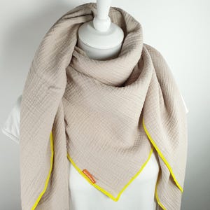 Puede incluir: Una bufanda de algod&oacute;n beige con ribete amarillo. La bufanda est&aacute; doblada y drapeada sobre un maniqu&iacute; blanco. El nombre de la marca "Wunderbar" es visible en la bufanda.